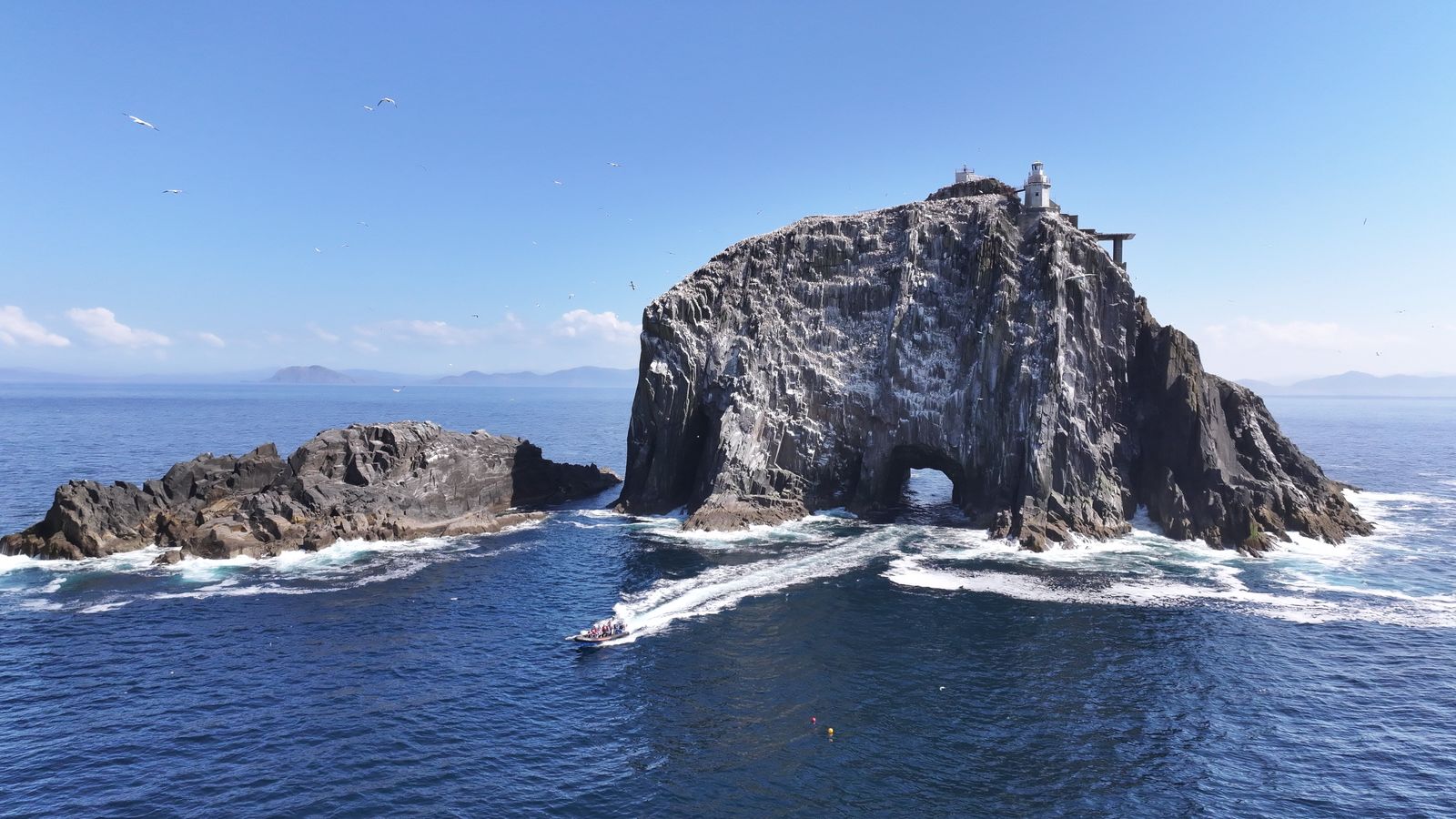PHOTO-2025-05-21-13-32-20 Boat approaching the Bull Rock sea arch beneath the historic lighthouse off the Beara Peninsula